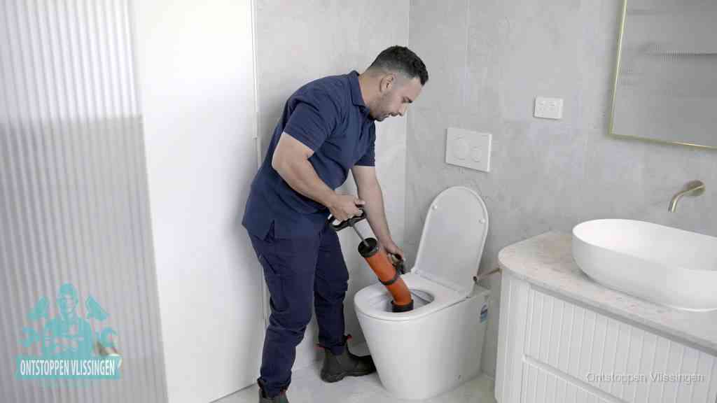 Een monteur buigt over een wandcloset en duwt met de hand een persluchtontstopper in de toiletpot om de verstopping handmatig los te maken in Vlissingen