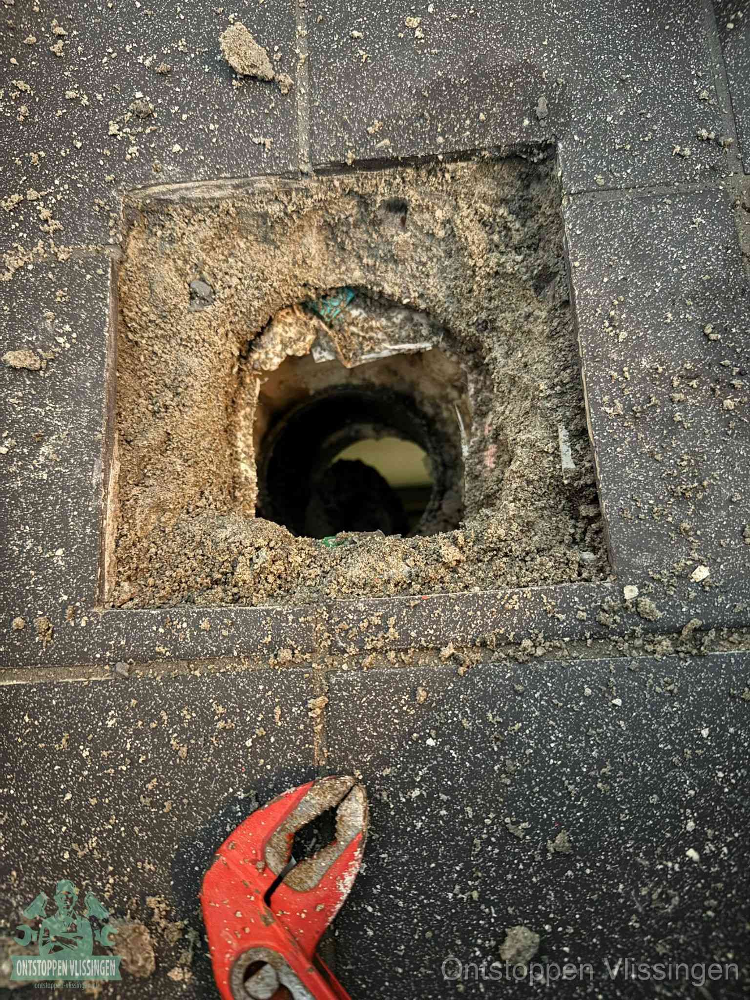 Een geopend rioolputje in een betontegelvloer met losgemaakt rooster en een zichtbare ronde afvoerbuis, het achterhalen waar de afvoerverstopping zit in Vlissingen
