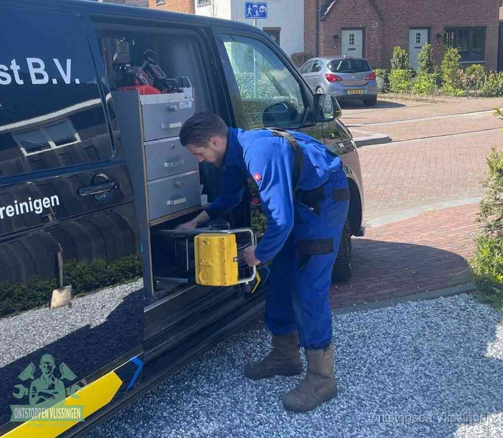 Een monteur pakt buiten op de oprit gereedschap uit de bedrijfsbus, het moment om een professional in te schakelen voor een verstopte afvoer in Vlissingen