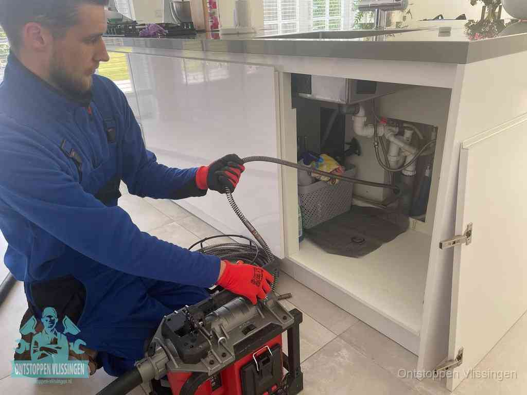 Monteur voert een ontstoppingsveer in de afvoer onder de keuken in Vlissingen