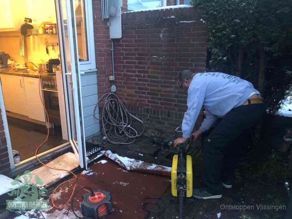 Een monteur werkt buiten bij een open riool-/grondput met een elektrische ontstoppingsmachine om een verborgen afvoerprobleem op te sporen in Vlissingen