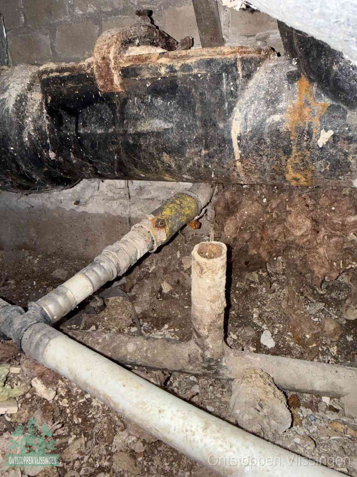 Een dikke zwarte hoofdrioolbuis met roest- en kalkaanslag in een kruipruimte, oorzaak van terugkerende structurele afvoerproblemen in Vlissingen