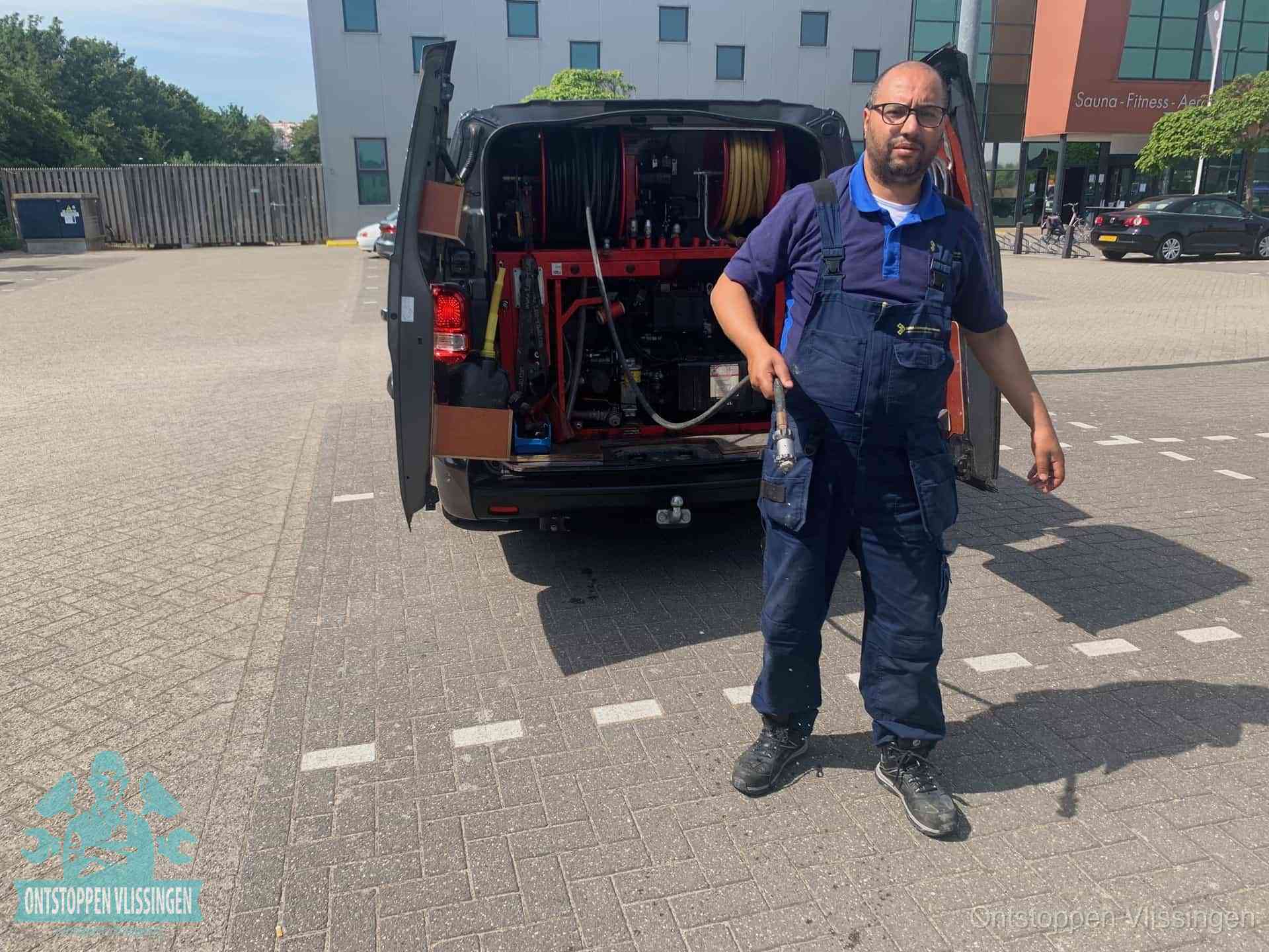 Een monteur bij zijn bestelbus met een hogedruk- en rioolreinigingsunit, klaar om de oorzaak van terugkerende wc-verstoppingen aan te pakken in Vlissingen