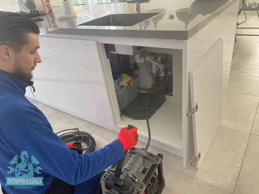 Monteur ontstopt met een veermachine een verstopte afvoer onder de gootsteen in Vlissingen
