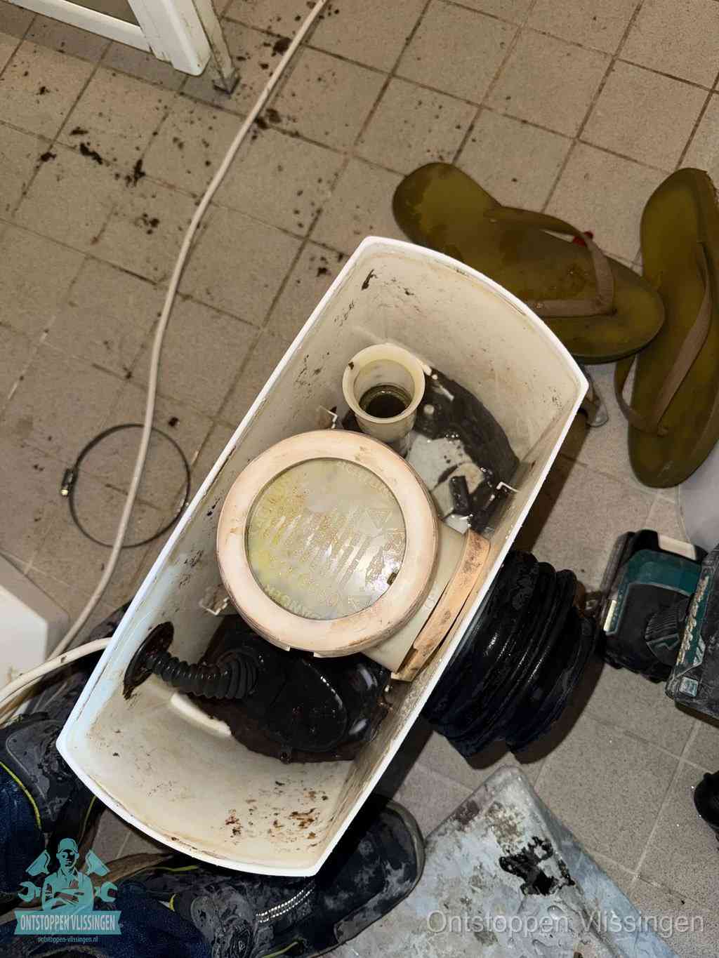 Een gedemonteerde toiletpot op de vloer met ontstoppingsveer en gereedschap ernaast, het verwijderen van een vastzittend voorwerp uit de wc in Vlissingen