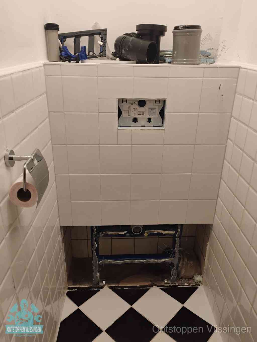 Een toiletruimte waar het hangtoilet en de inbouwreservoir-onderdelen zijn vrijgelegd voor onderhoud, periodiek nazicht voorkomt een wc-verstopping in Vlissingen
