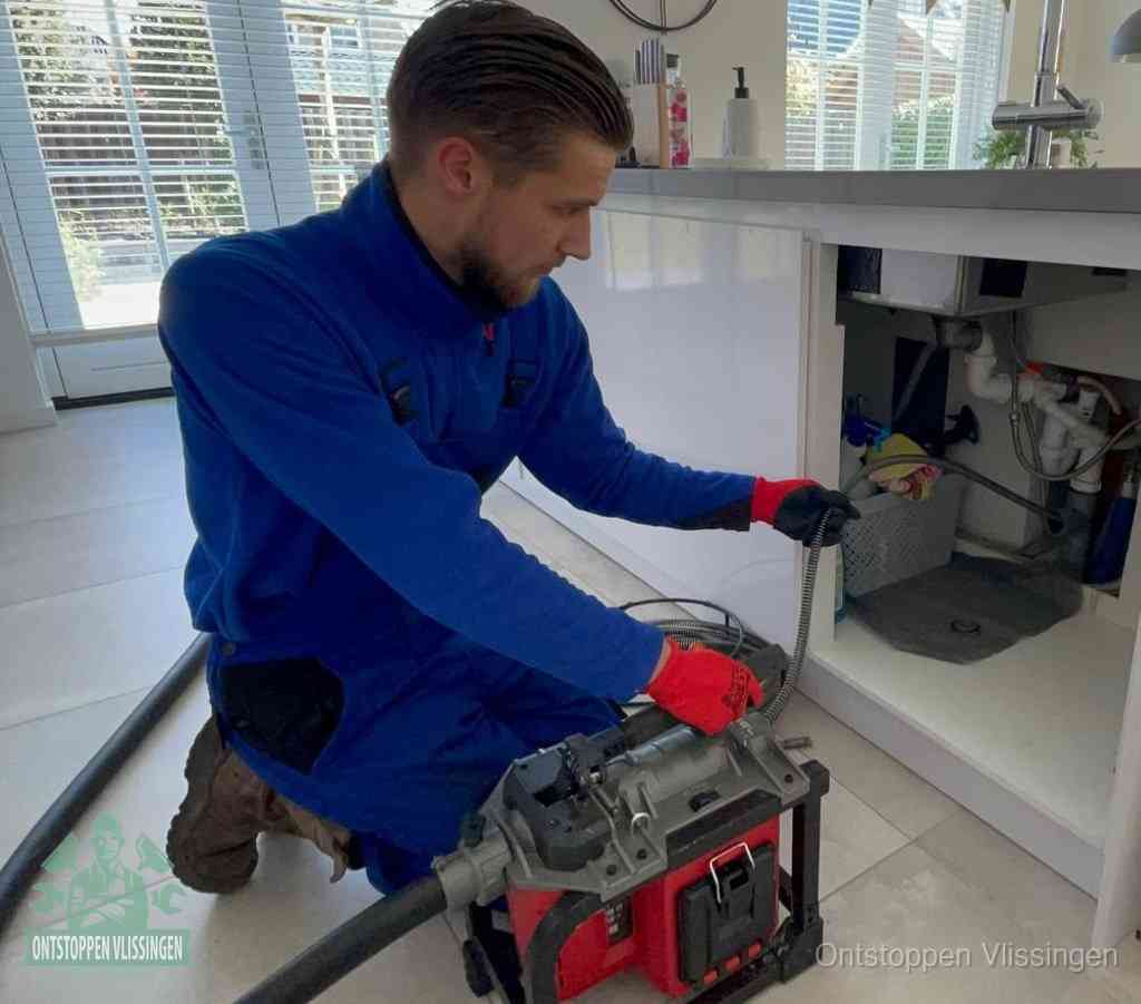 Een monteur met rode handschoenen knielt in een keuken en voert een elektrische ontstoppingsveer in tijdens het professioneel afvoer ontstoppen in Vlissingen