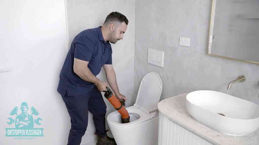 Een man gebruikt een handmatige luchtdruk-ontstopper in een modern betegeld toilet om zelf de wc te ontstoppen in Vlissingen